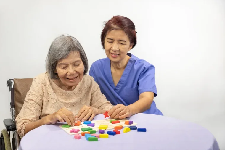 A caregiver doing a shape-puzzle activity with a senior woman