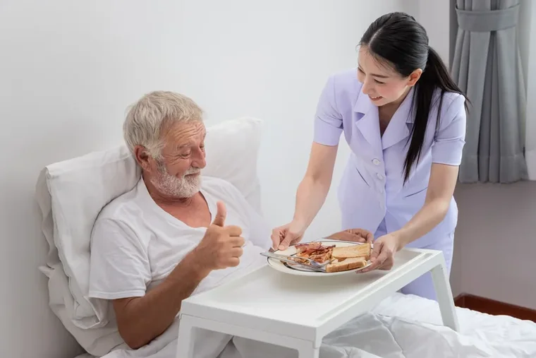 A caregiver serving a smiling senior man breakfast in bed