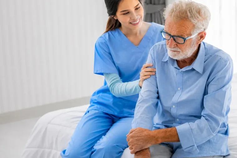 A caregiver supporting a senior man with a reassuring hand on his shoulder