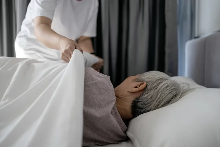 A caregiver helping a senior settle comfortably in bed